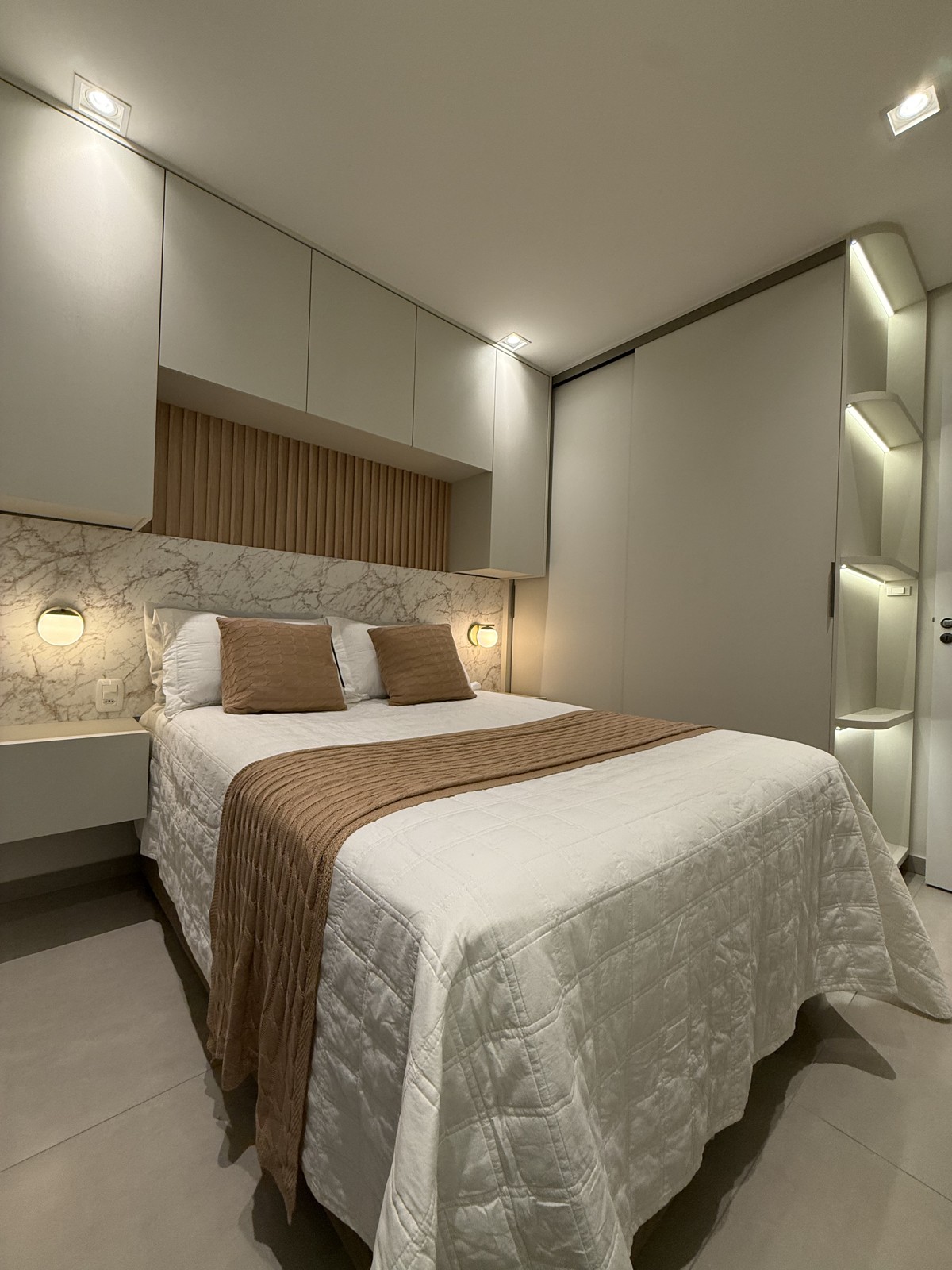 Dormitório com cama, cabeceira com painel ripado, armários claros e nichos iluminados