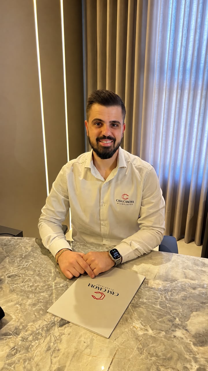 Felipe, da Casa Canova Planejados, sentado à mesa do escritório com a camisa da marca