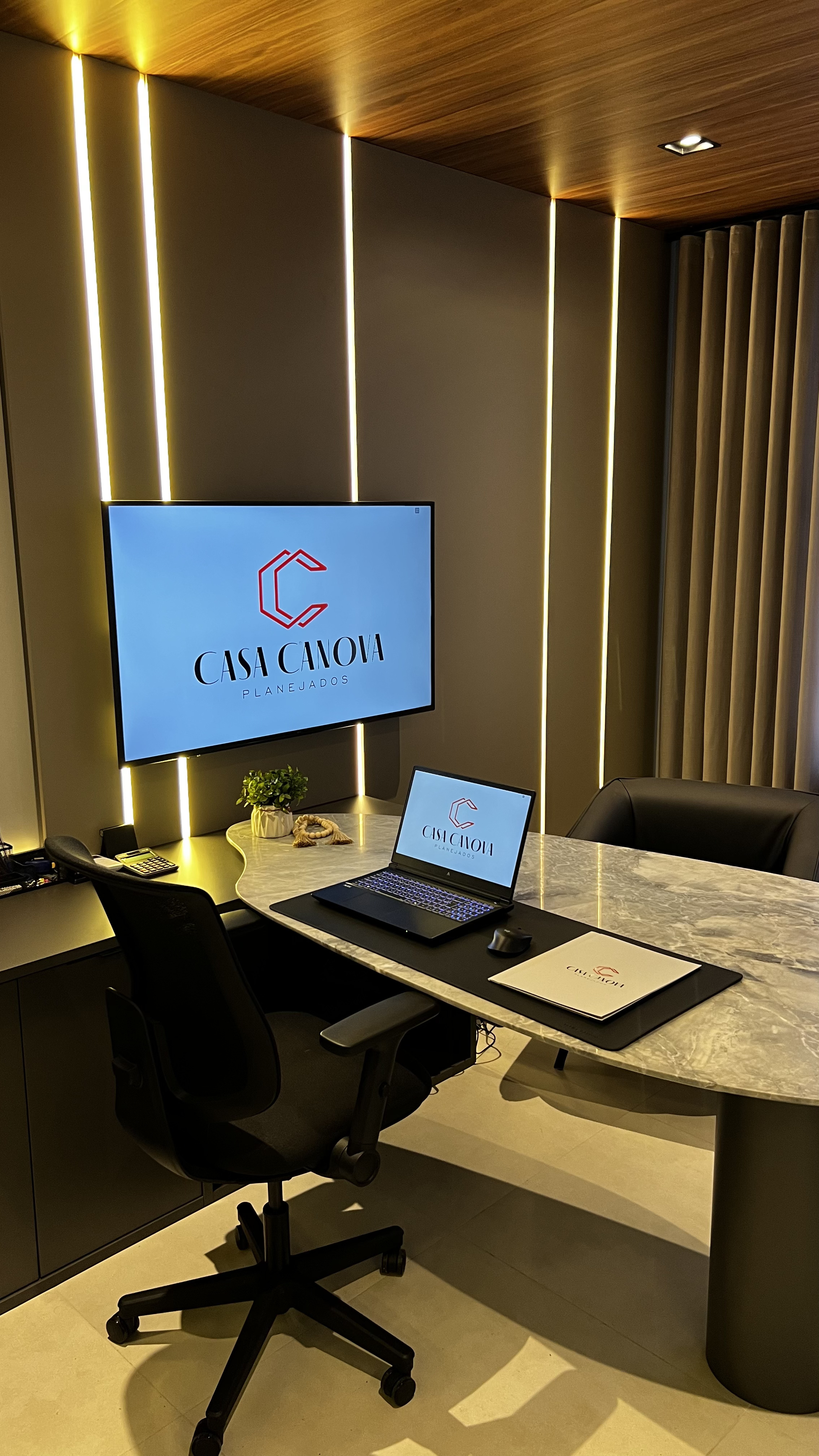 Sala de reunião corporativa da Casa Canova com marcenaria, mesa de mármore e telas com a marca